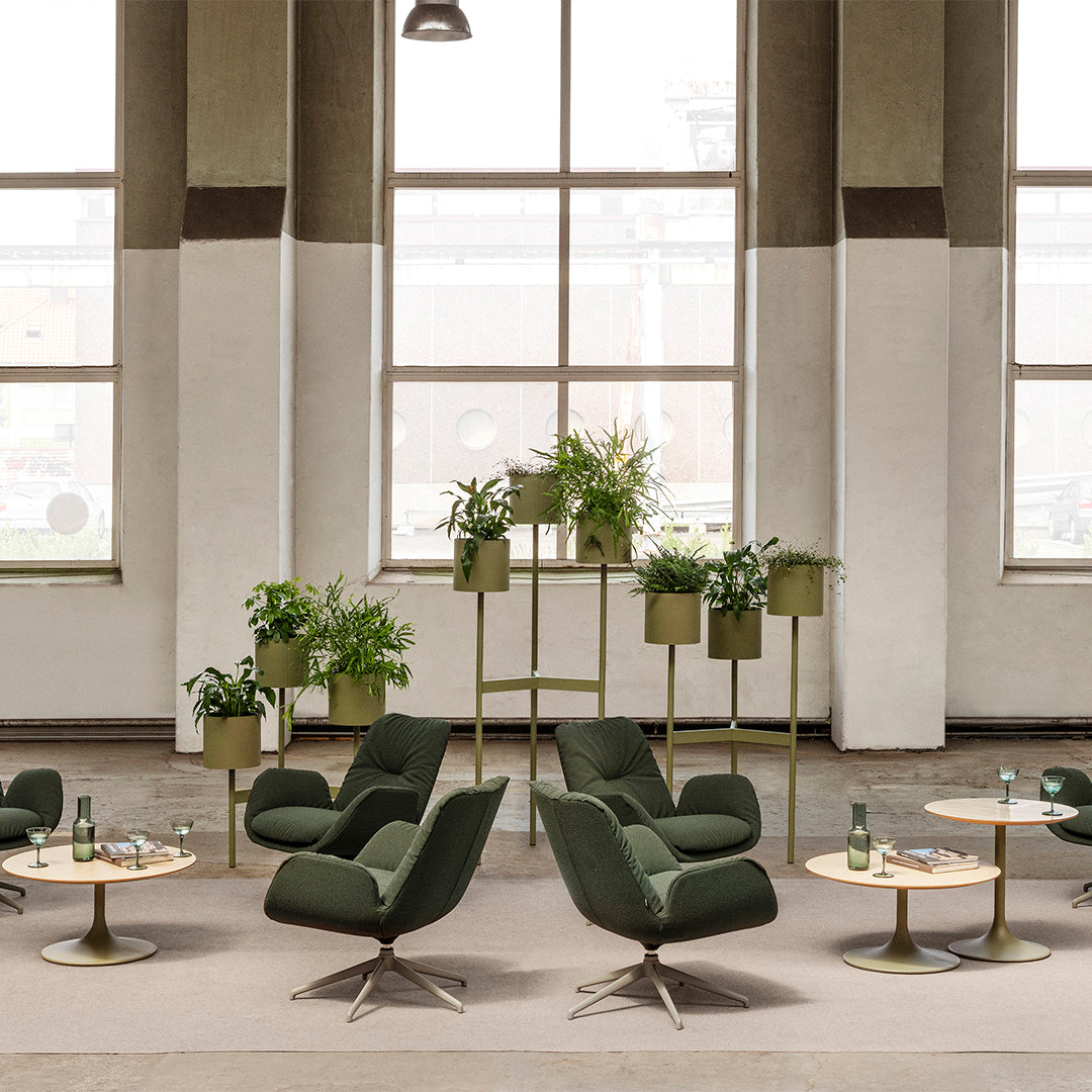 Green patterned chairs with light wood tables, complemented by greenery in muted planters against a neutral backdrop.