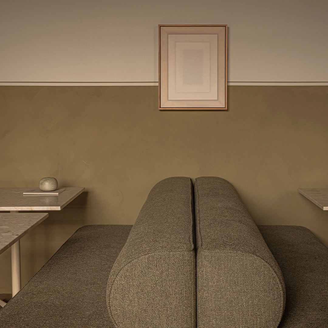 Soft olive green wall with a textured gray couch, complemented by minimalist white artwork and light marble tables.