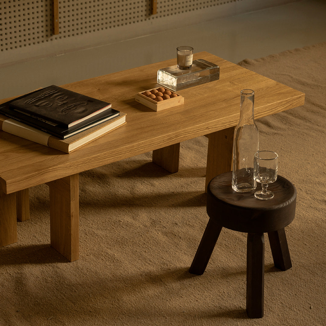 "Natural wood coffee table with a dark wooden stool, featuring a neutral beige rug and subtle decorative elements."