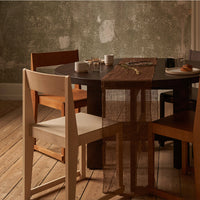 Elegant brown table runner on a dark wood table, surrounded by light and dark wooden chairs, against a muted green wall.