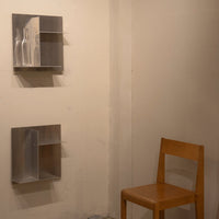 Minimalist gray shelves on a beige wall with a natural wood chair, emphasizing clean lines and subtle contrast.