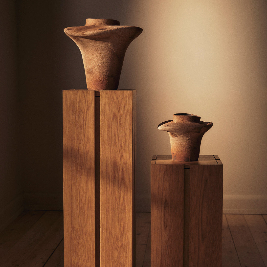 Terracotta vases with natural earthy tones and unique swirling patterns, displayed on sleek wooden pedestals.