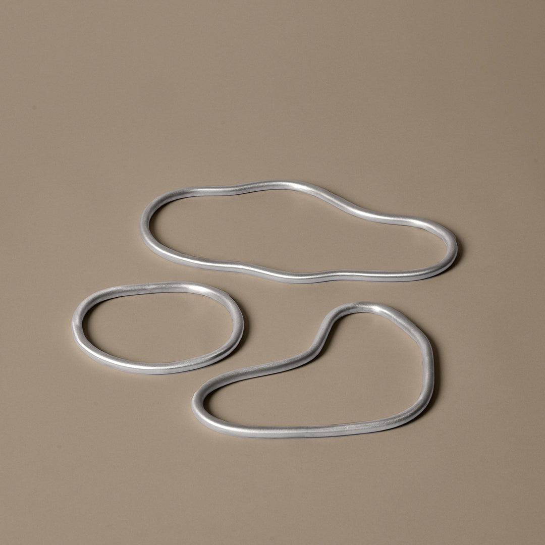 Silver metal shapes on a soft beige background, showcasing fluid, organic forms and contemporary design.