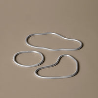 Silver metal shapes on a soft beige background, showcasing fluid, organic forms and contemporary design.