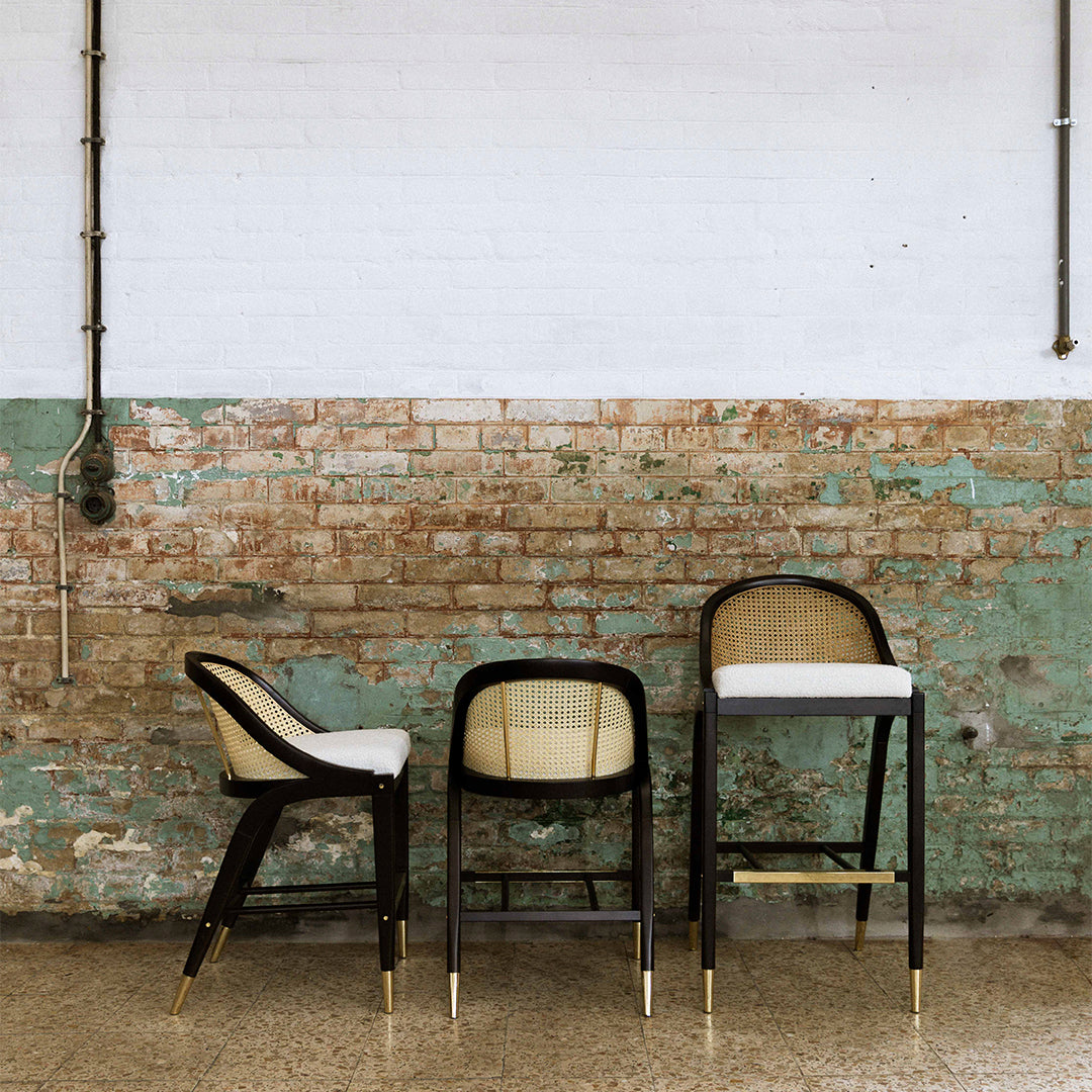 Three stylish bar stools in black, beige, and white against a textured distressed green and brick wall.