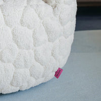Textured white cushion with a honeycomb pattern and a small pink tag on a blue-gray surface.