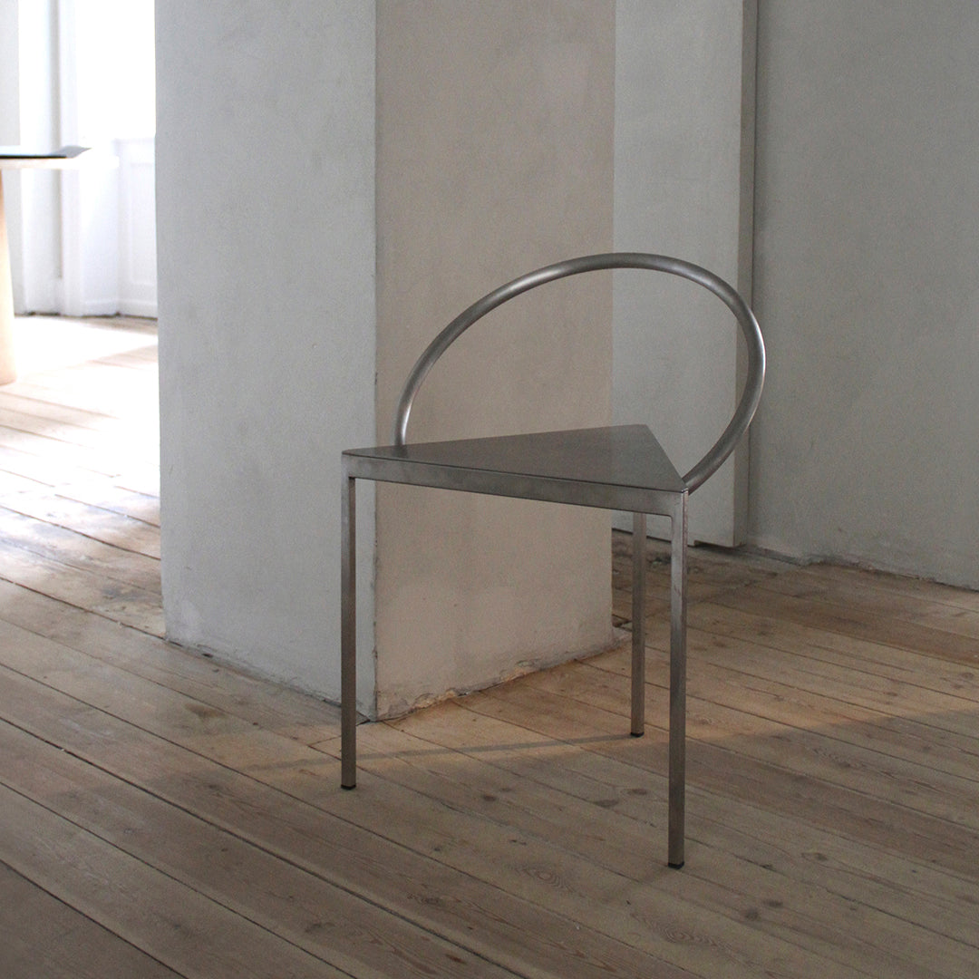 Modern triangle chair with sleek silver metal design and unique circular backrest in a minimalistic interior setting.