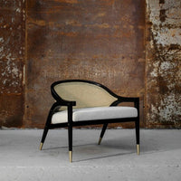 Elegant black and natural rattan chair with a white cushioned seat, featuring gold accents and a sleek design.