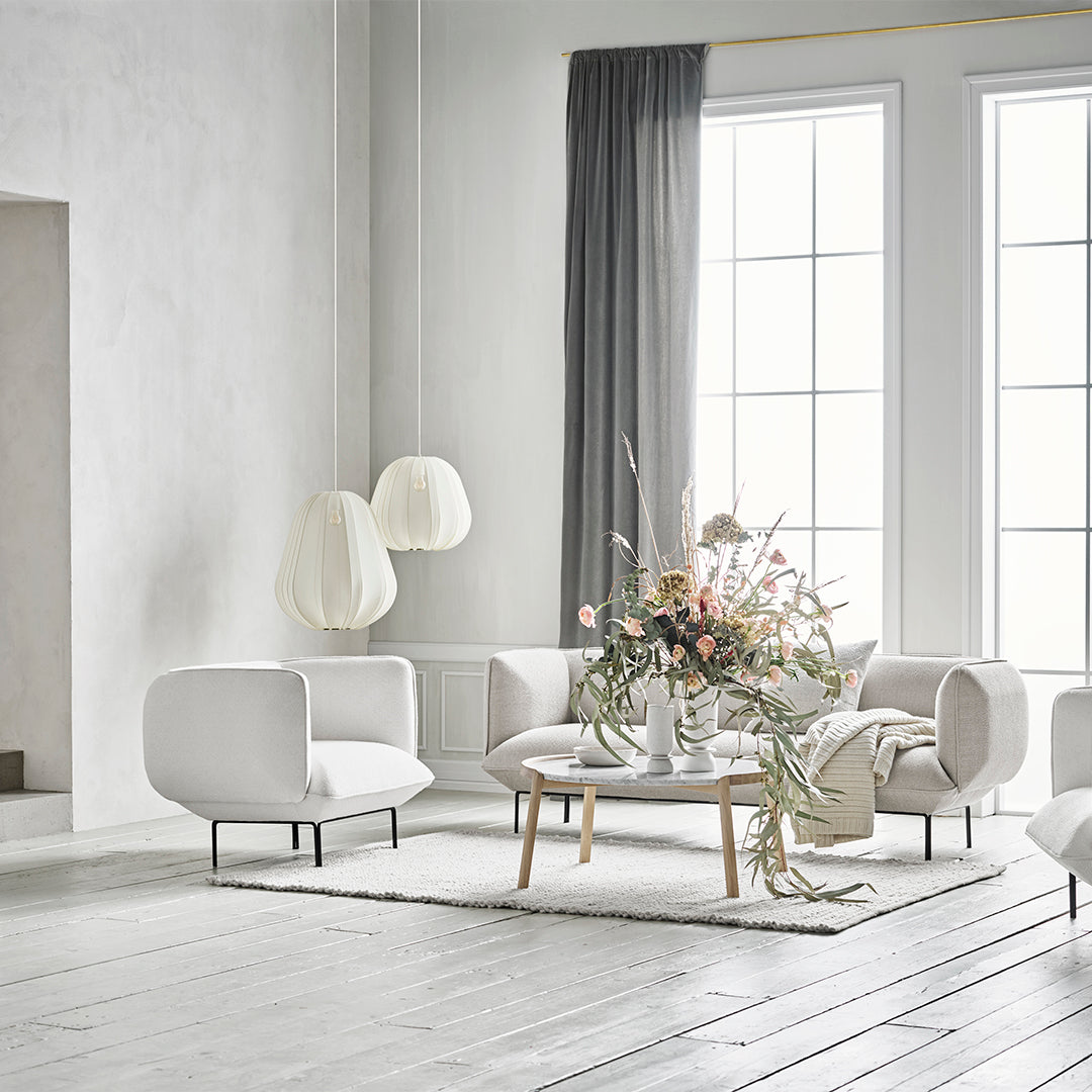Modern living room featuring soft white furniture, gray curtains, and a floral arrangement in pastel hues.