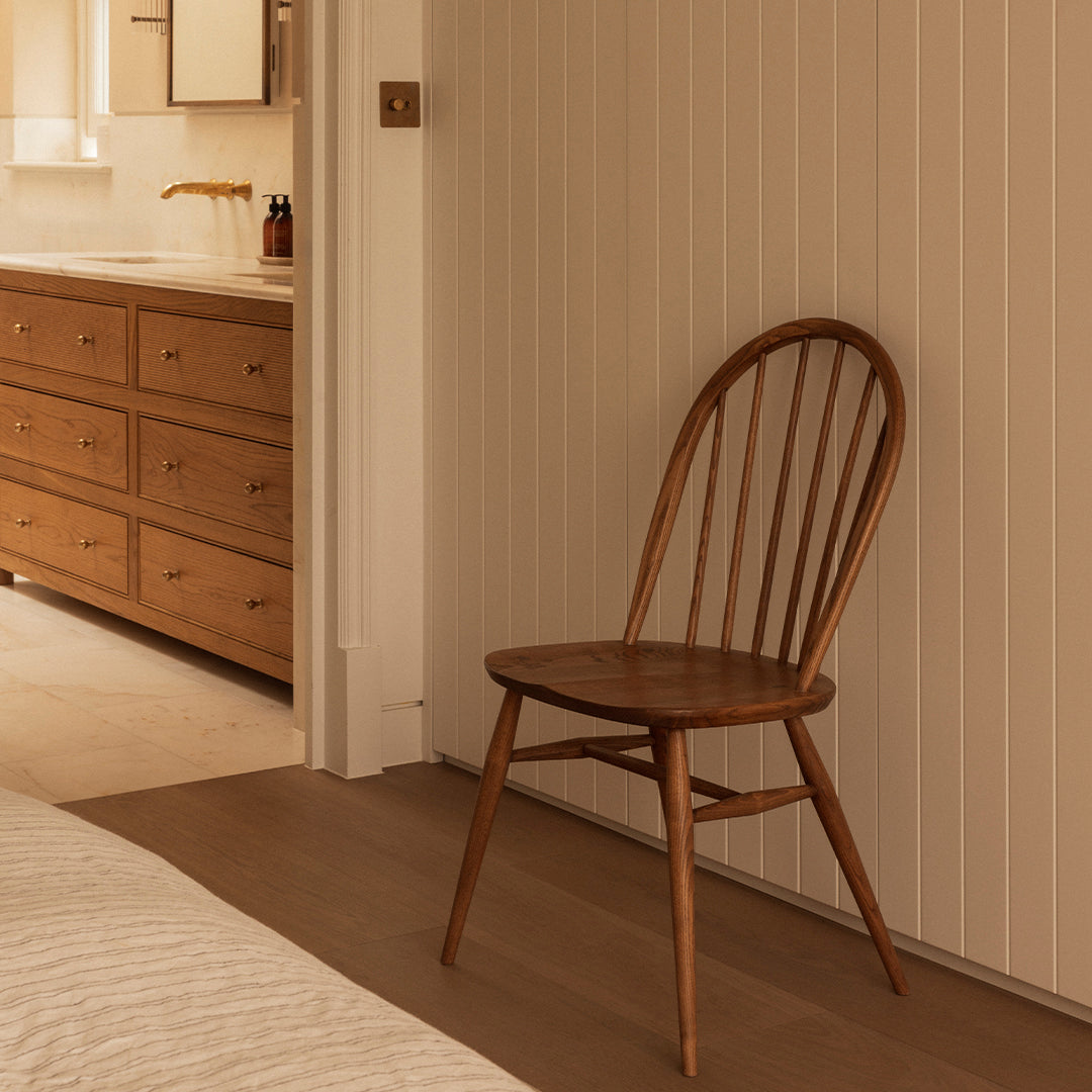 Wooden chair in warm brown tones, featuring a classic spindle-back design against a neutral-colored wall.