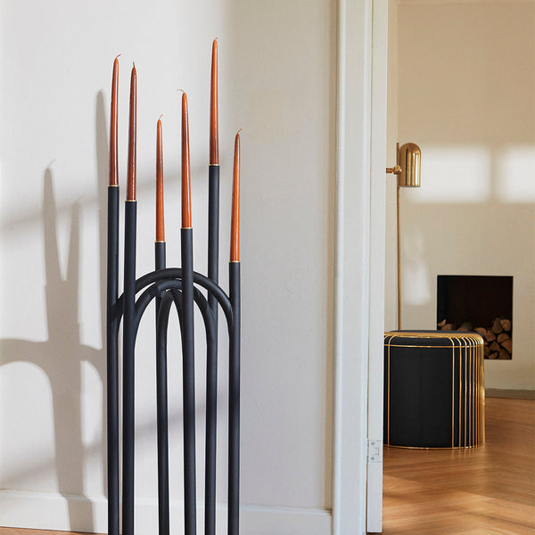 Black candle holder with copper-tipped candles, featuring sleek lines and minimalist design against a neutral backdrop.