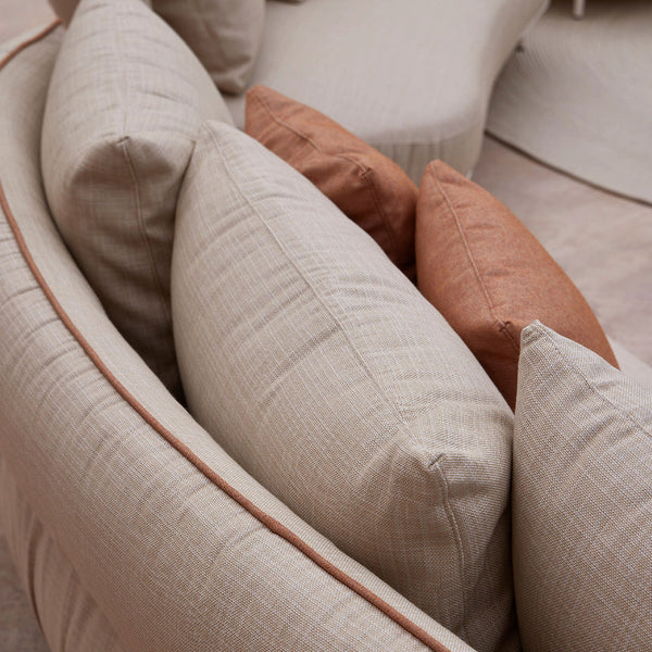 Beige and terracotta decorative pillows with subtle texture, arranged on a curved sofa. Cozy, modern design elements.