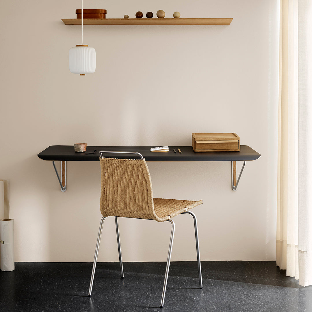 Wall-mounted black desk with natural wood accents and a woven chair against a soft beige wall. Bright and minimal design.