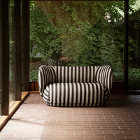 Black and white striped sofa with a rounded design, set against a natural backdrop. Elegant, modern pattern.