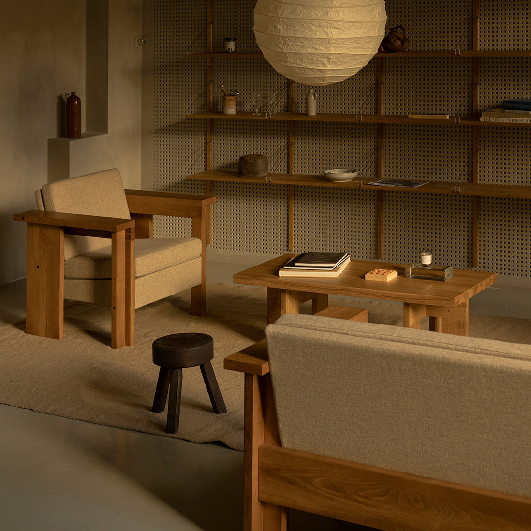 Neutral beige armchairs and a wooden table against a soft, earthy backdrop with a textured rug and warm lighting.