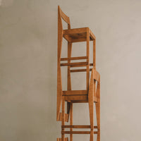 Stacked wooden stools in warm oak finish with minimalistic design and clean lines against a neutral background.