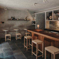 "Modern bar setting featuring dark gray stone flooring, light wood accents, and warm metallic lighting."