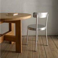 Silver metal chair beside a wooden table on a light wood floor, featuring a minimalist design.