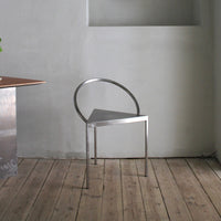 Minimalist metal chair with a sleek silver finish and unique triangular design against a soft gray background.