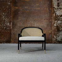 Black and beige chair with woven cane backrest and white cushion, complemented by gold accents.