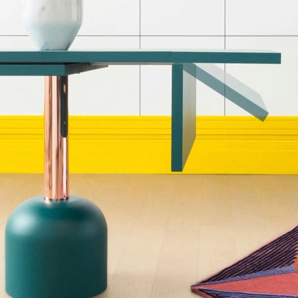 Teal table with copper accents and a vibrant yellow backdrop, featuring geometric patterns on the surrounding rug.