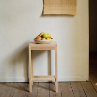 Light wood side table with a smooth finish, featuring a round bowl filled with colorful fruits.