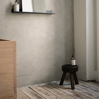 Minimalist design featuring a textured gray wall, light wooden floor, and a dark wooden stool. Elegant and modern colors.