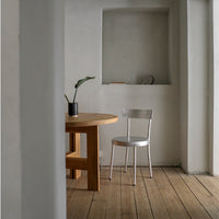 Minimalist room with a natural wood table, silver chair, and neutral gray walls, featuring warm wooden floorboards.