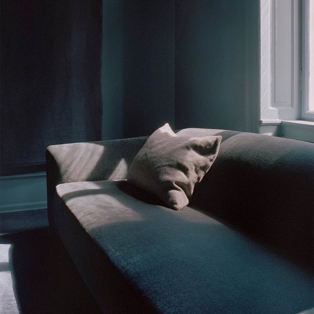 Dark blue couch with a light gray pillow, bathed in soft natural light. Elegant and modern texture.
