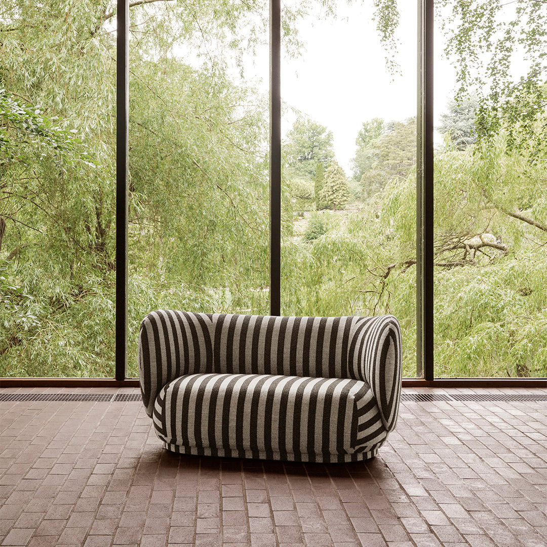 Black and white striped sofa with a unique design, set against a backdrop of lush greenery.