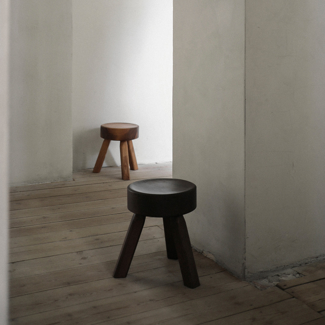 Two wooden stools: one dark brown with a simple round top, and one light brown, showcasing natural wood grain patterns.