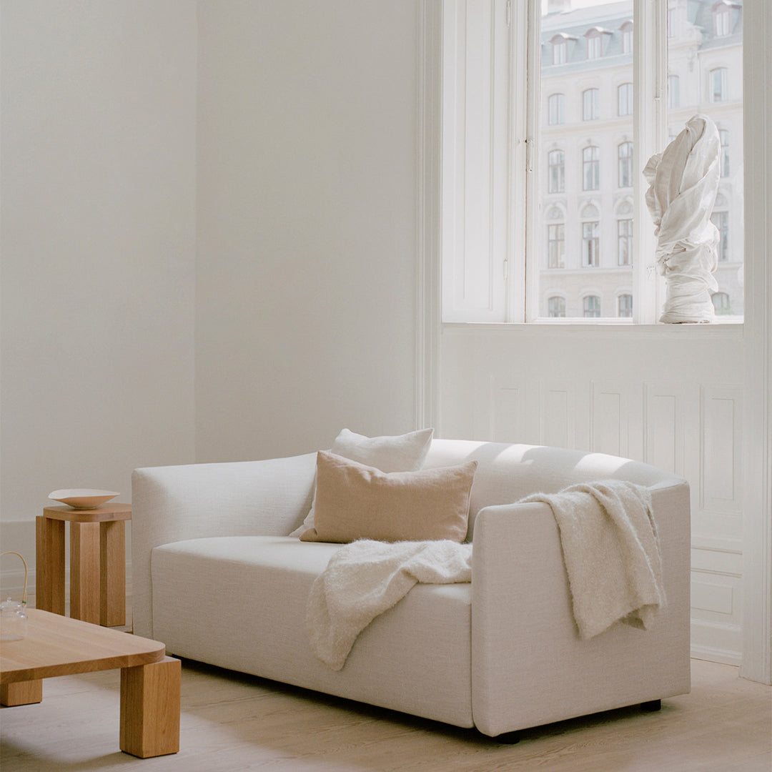 Minimalist white sofa with soft beige pillows and a cozy throw, set in a light-filled room with neutral tones.