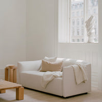 Minimalist white sofa with soft beige pillows and a cozy throw, set in a light-filled room with neutral tones.