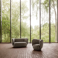 Black and white striped sofa and chair in a bright, airy setting with large windows and greenery outside.