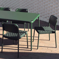 Green rectangular table with black woven pattern chairs, showcasing a modern design and contrasting colors.