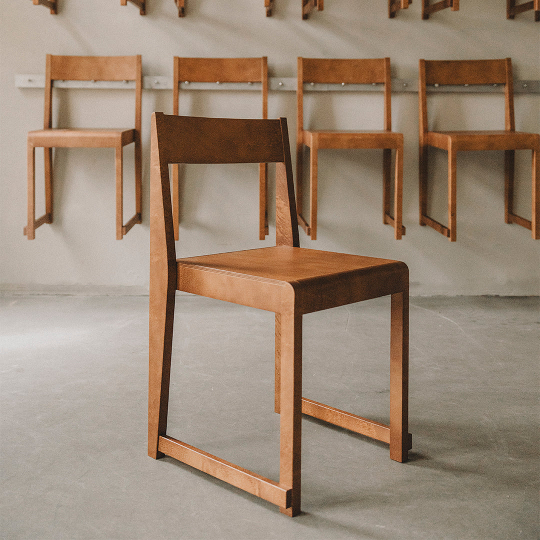 "Minimalist wooden chair in warm brown hue, showcasing a smooth, sleek finish against a light grey background."
