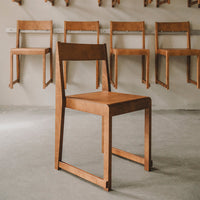 "Minimalist wooden chair in warm brown hue, showcasing a smooth, sleek finish against a light grey background."