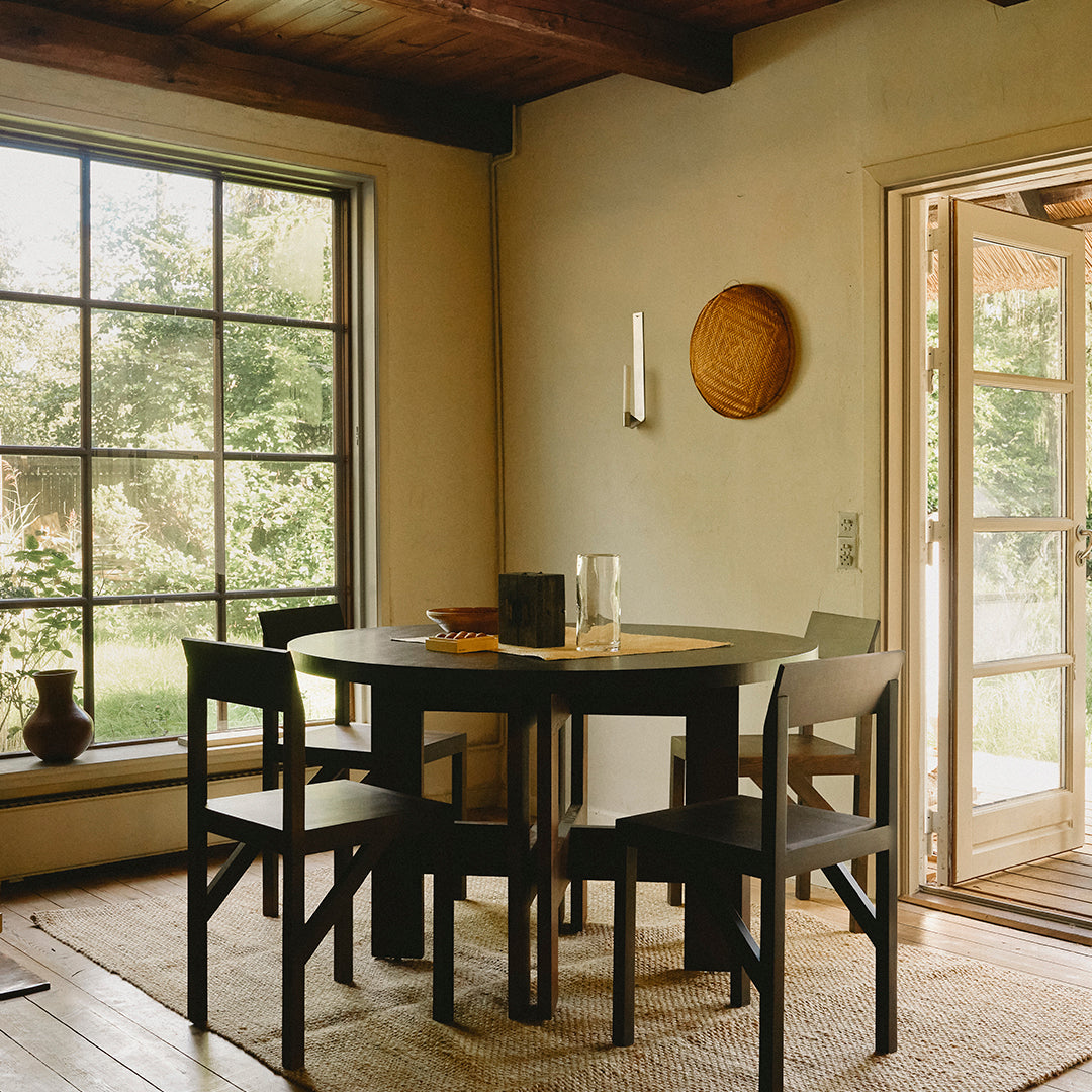 Black wooden table with matching chairs, earthy tones and natural textures, complementing sunlight through large windows.