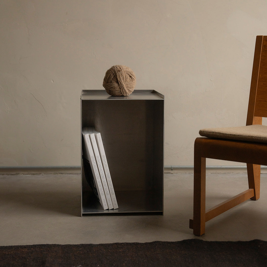 Modern metallic side table in sleek grey with minimalistic design, complemented by natural wood chair and earthy tones.
