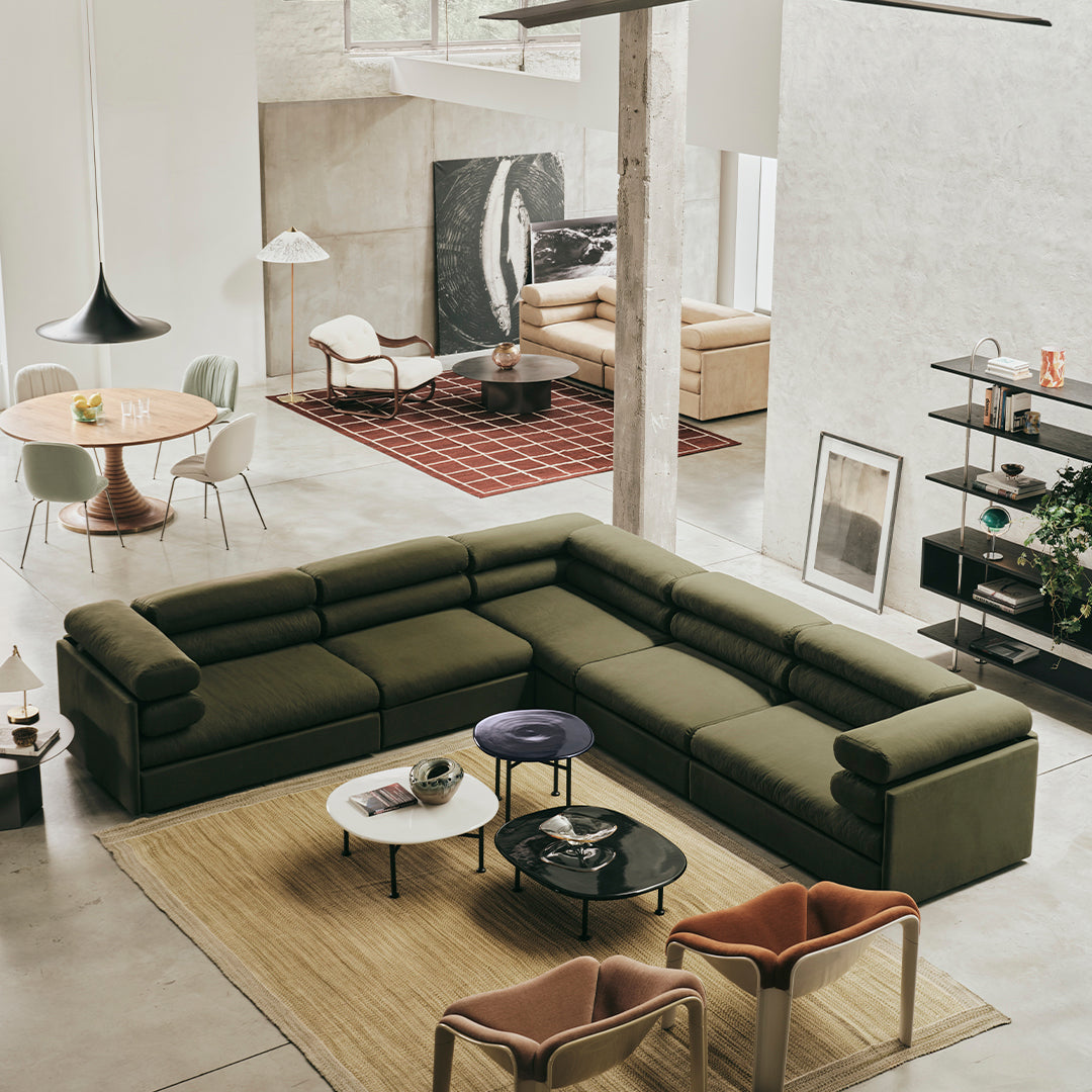 Olive green sectional sofa with a textured fabric, paired with colorful accent chairs and a neutral rug in a modern living space.
