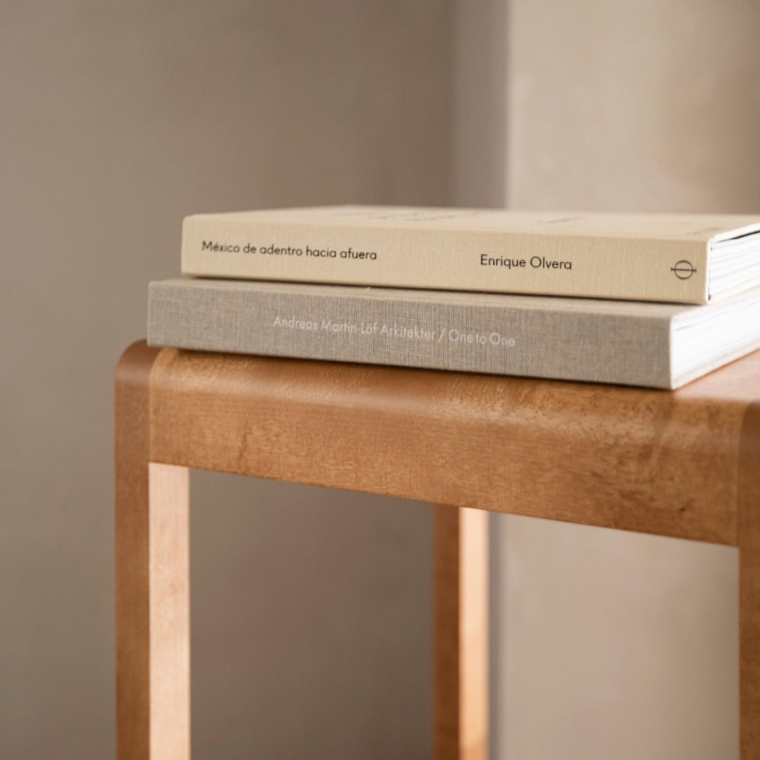 Stack of neutral-toned books in beige and light gray on a warm, wooden table surface with a smooth finish.