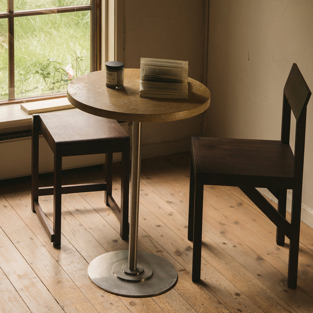 Round wooden table with a natural finish, paired with dark brown wooden chairs, set against a serene, light-filled background.