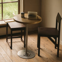 Round wooden table with a natural finish, paired with dark brown wooden chairs, set against a serene, light-filled background.