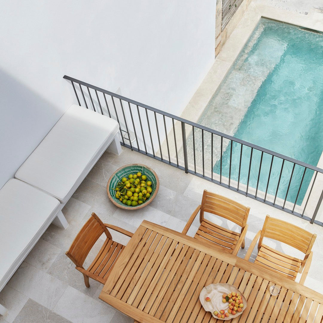 Minimalist outdoor patio with white seats, natural wood furniture, and a vibrant green bowl of lemons beside a clear pool.