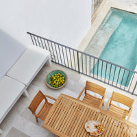 Minimalist outdoor patio with white seats, natural wood furniture, and a vibrant green bowl of lemons beside a clear pool.