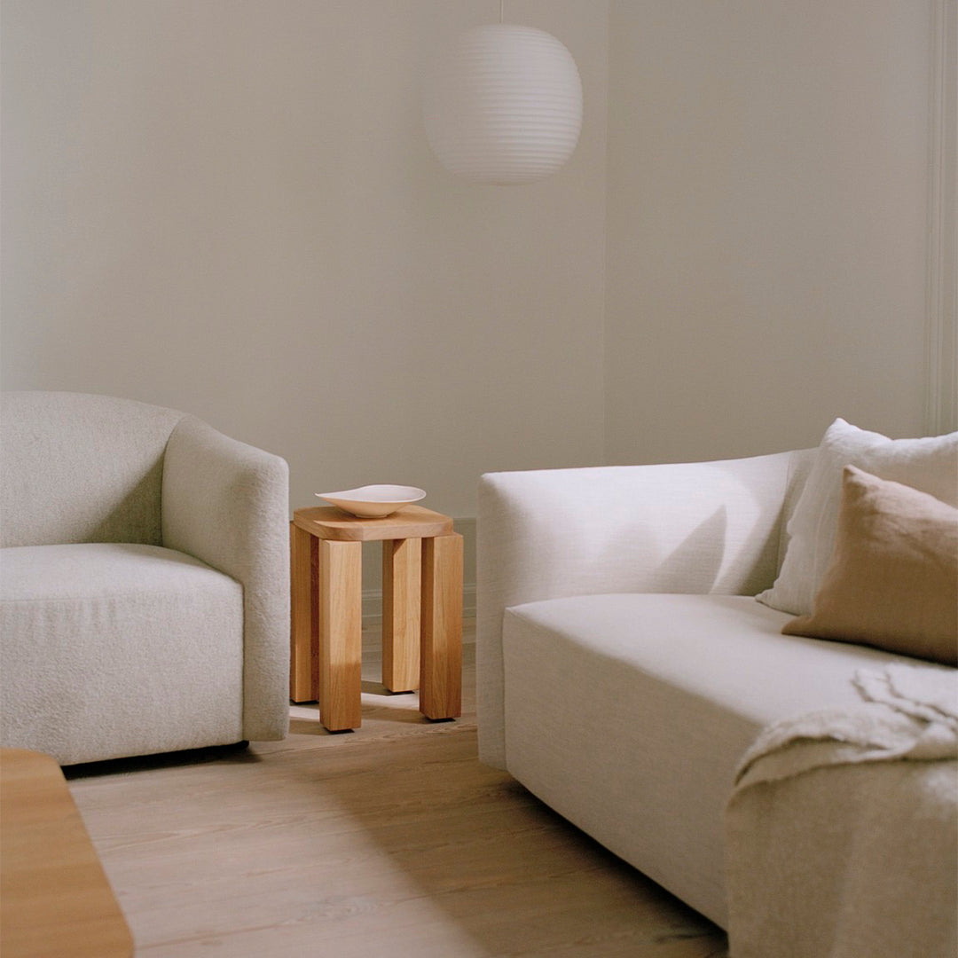 Light beige sofas with soft textures, warm wooden side table, and minimalistic decor create a cozy, neutral living space.