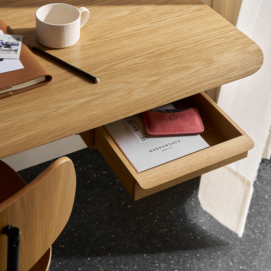 Light wood desk with a smooth finish, featuring a hidden drawer and a minimalist design, complemented by warm orange accents.