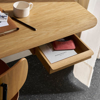 Light wood desk with a smooth finish, featuring a hidden drawer and a minimalist design, complemented by warm orange accents.