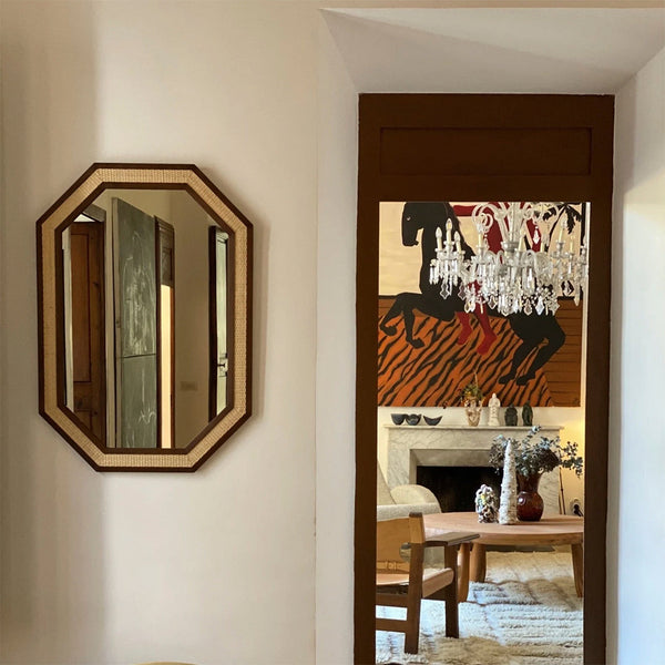 Octagonal mirror with brown trim and natural woven accents, reflecting bold black and orange patterns in the background.