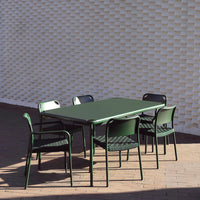 Rectangle green dining table with black slatted chairs against a textured white wall.
